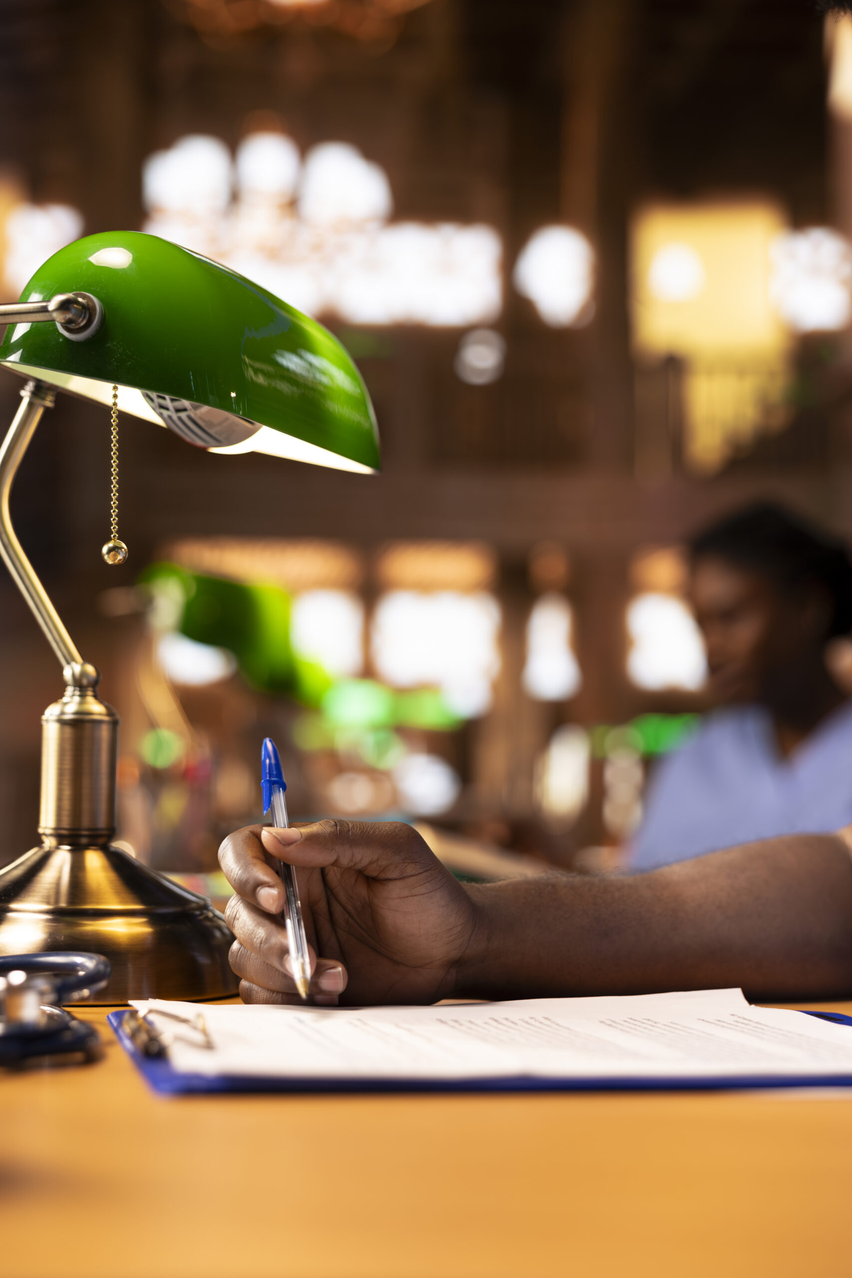 Black med student in scrubs does research and takes notes for his thesis, working hard at the campus library to become a doctor and obtain his diploma. Young man studying from books. Close up.